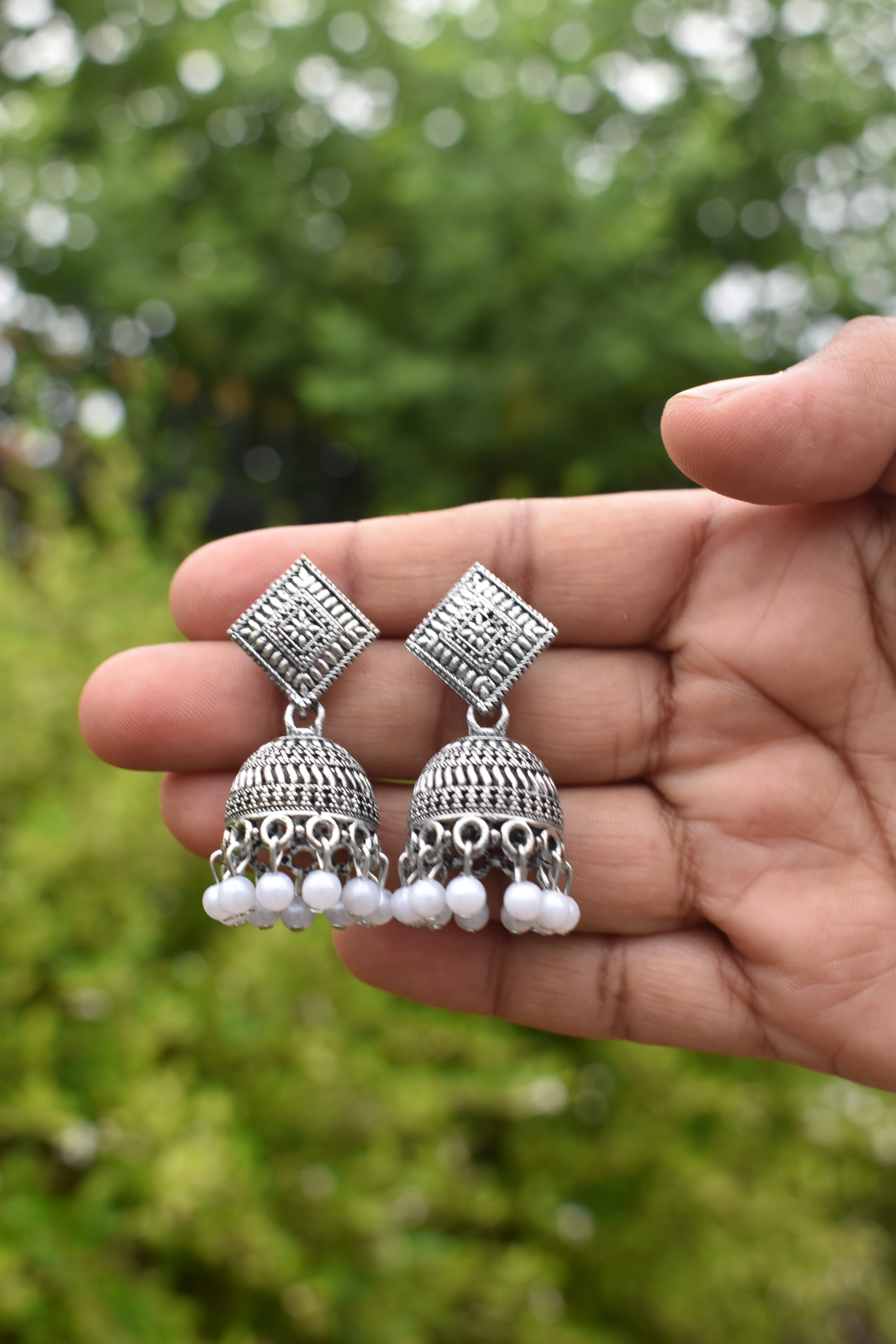 Jhumka held in a hand against a blurred green background